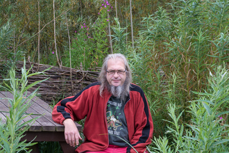 Mark sat on a bench surrounded by trees 